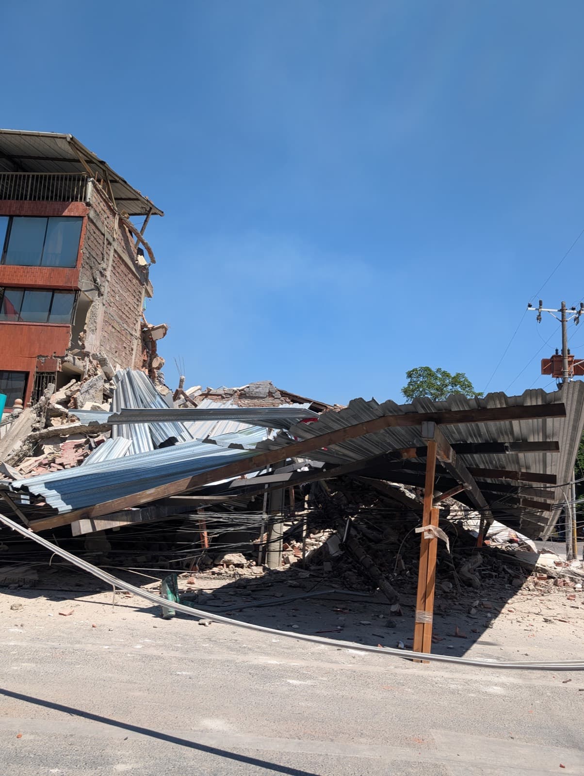 A brick building with one corner collapsed, its corrugated metal roof buckled down onto the street below.
