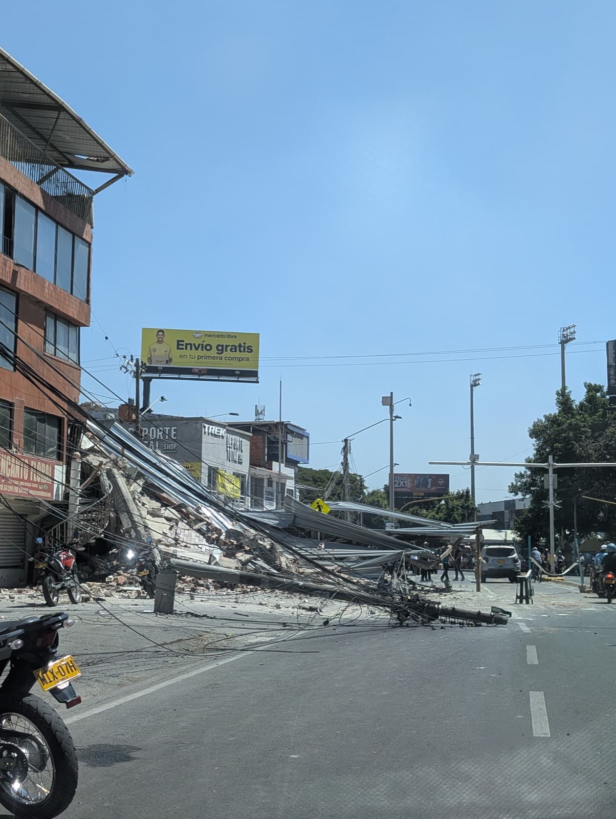 A street strewn with fallen power lines and a toppled utility pole, beside a building that has collapsed onto the pavement.